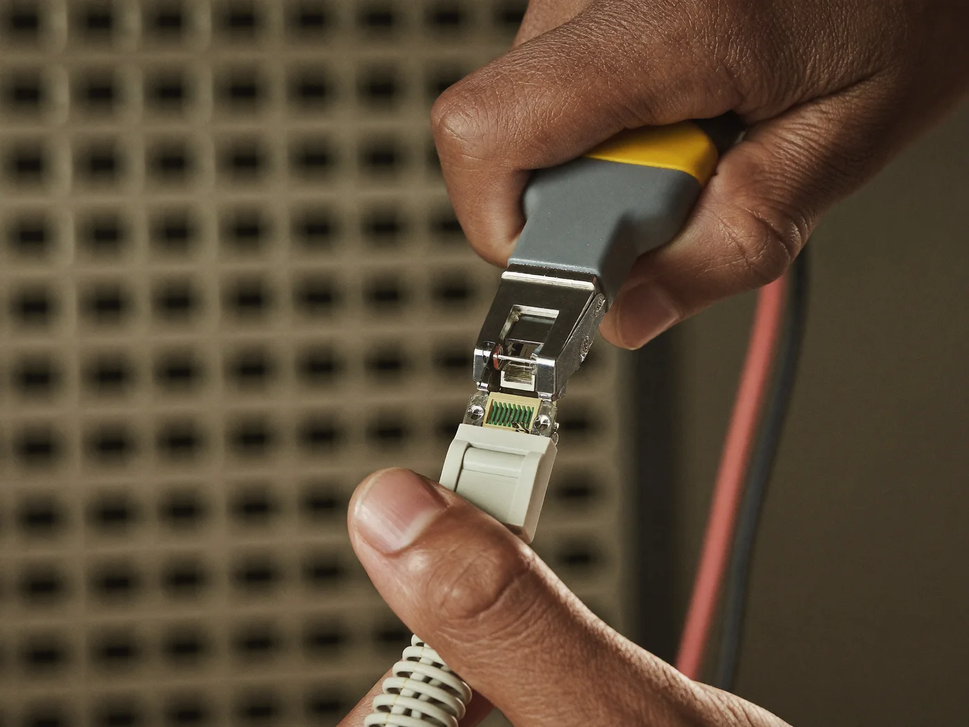 Hand crimpt einen RJ45-Stecker an ein Netzwerkkabel, im Hintergrund ein unscharfes Patchpanel