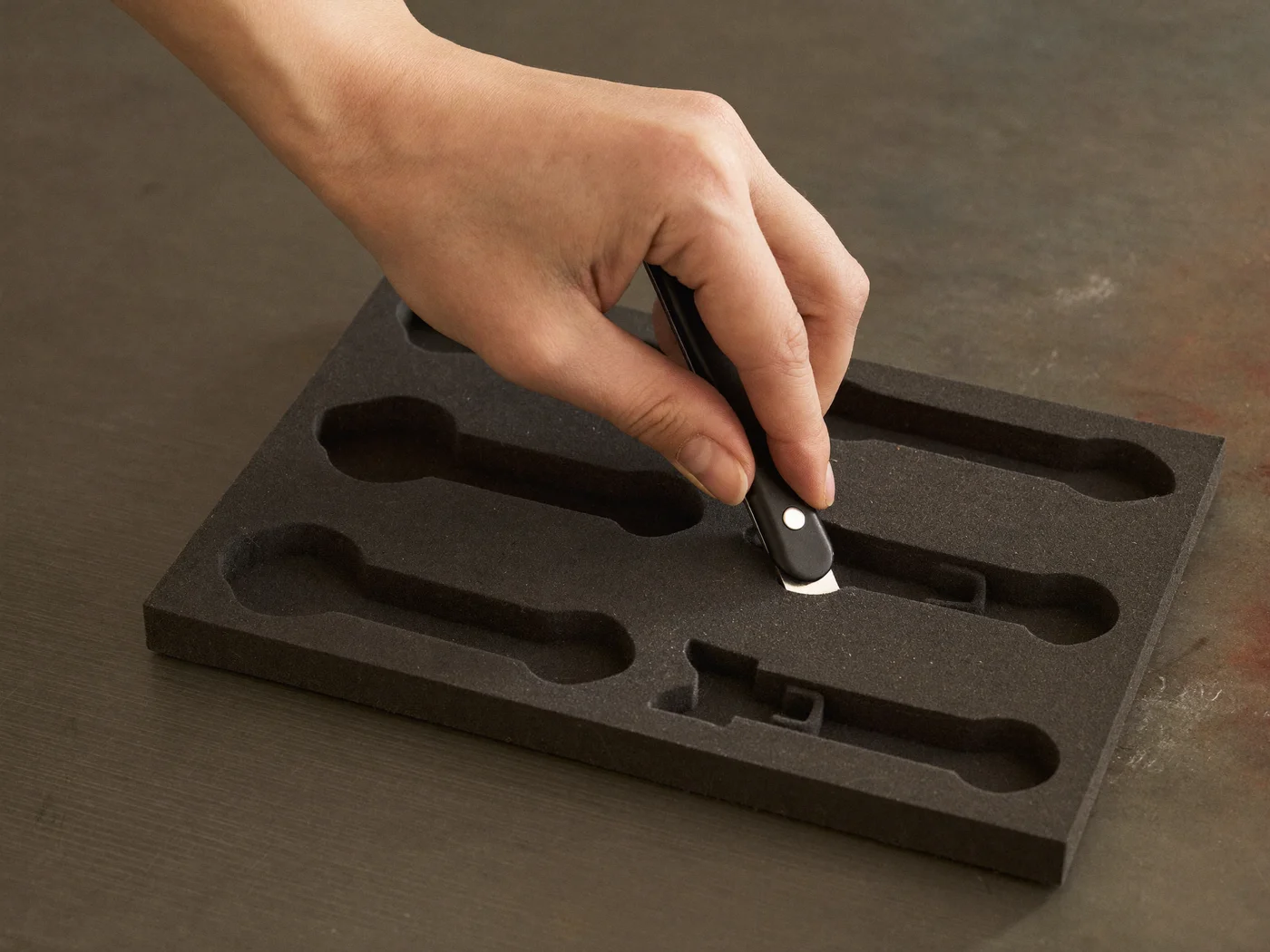 Hand schneidet mit einem Cutter-Messer eine Schaumstoff-Werkzeugeinlage zu